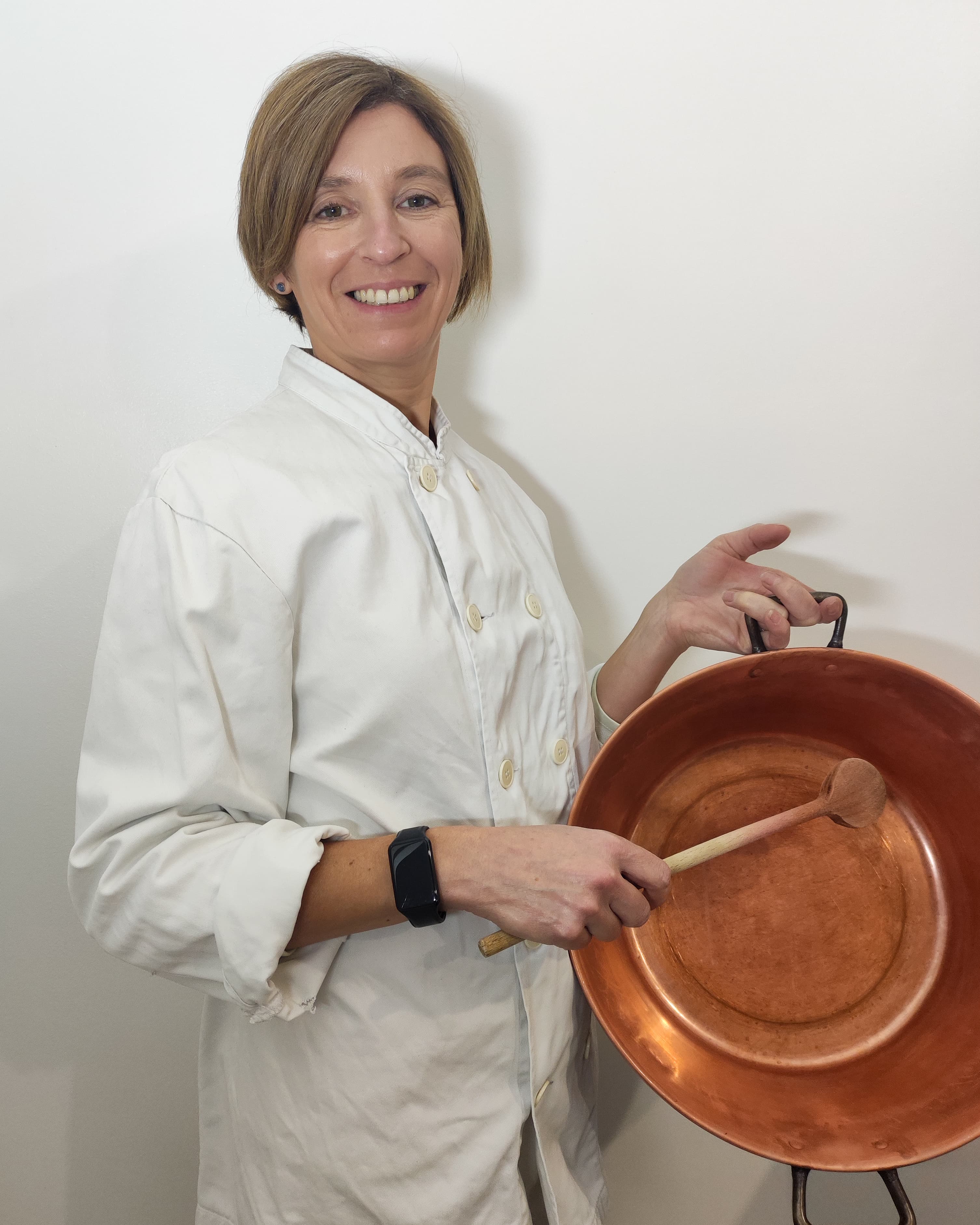 Guilaine souriante, en veste de cuisine, avec sa bassine à confiture en cuivre